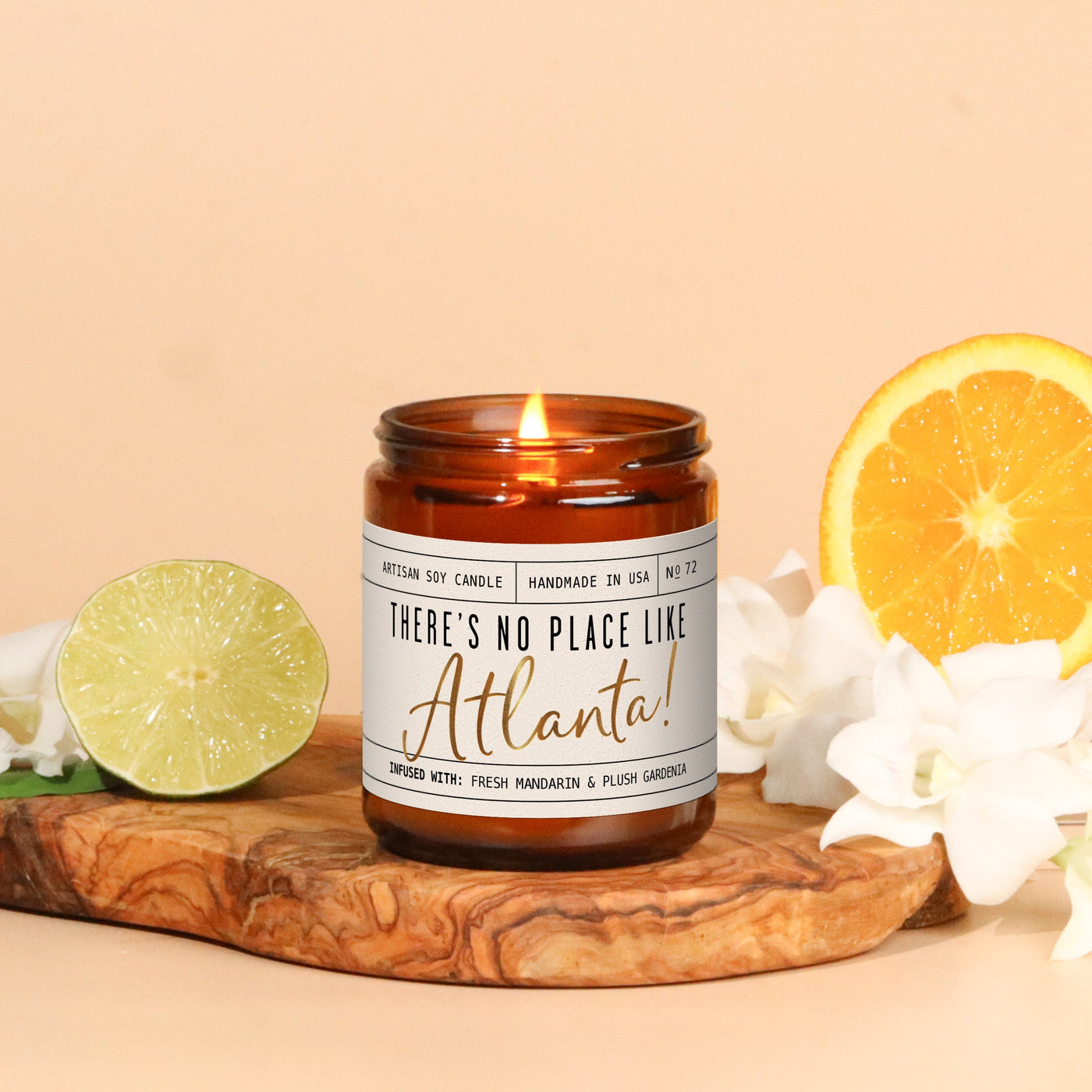 Candle labeled 'There's No Place Like Atlanta' on a wooden board with citrus fruits and flowers on a beige background
